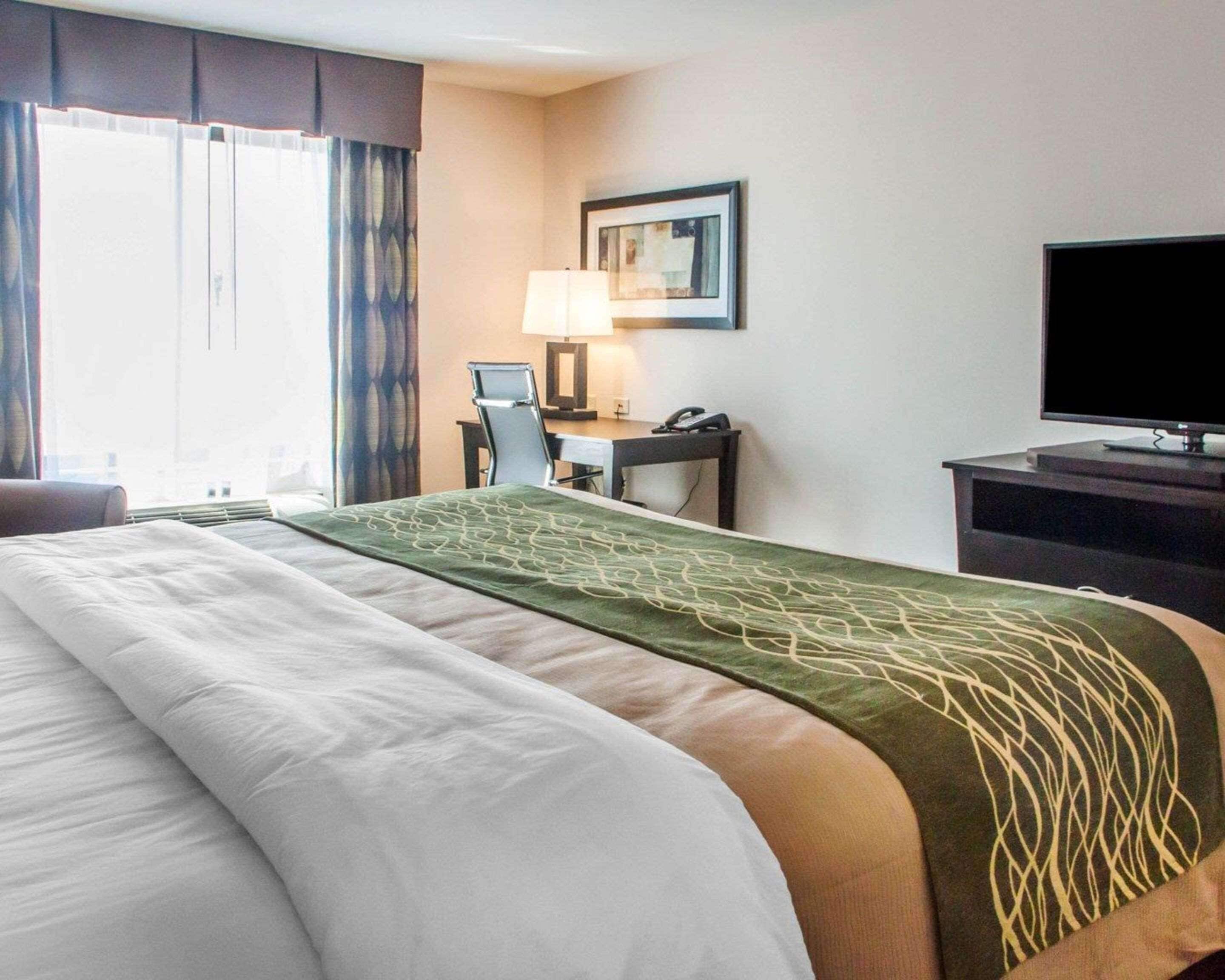 A hotel room with a large bed, a desk with a computer, a chair, a television, and a window with curtains.