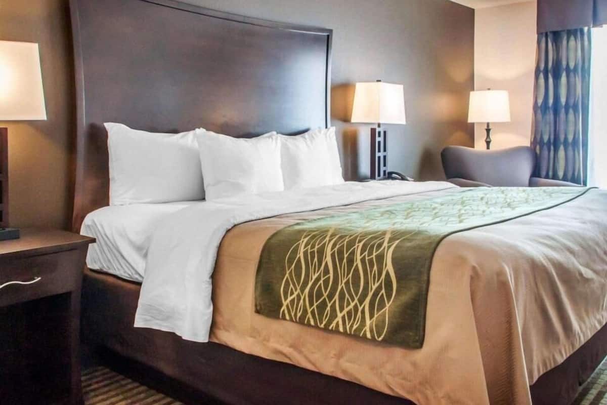 A hotel room with a large bed, two bedside tables, a chair, and a window with curtains.