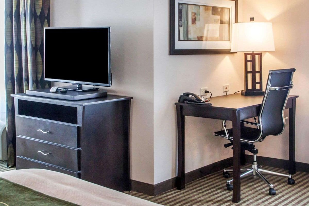 A hotel room with a desk, chair, television, and a framed picture on the wall.