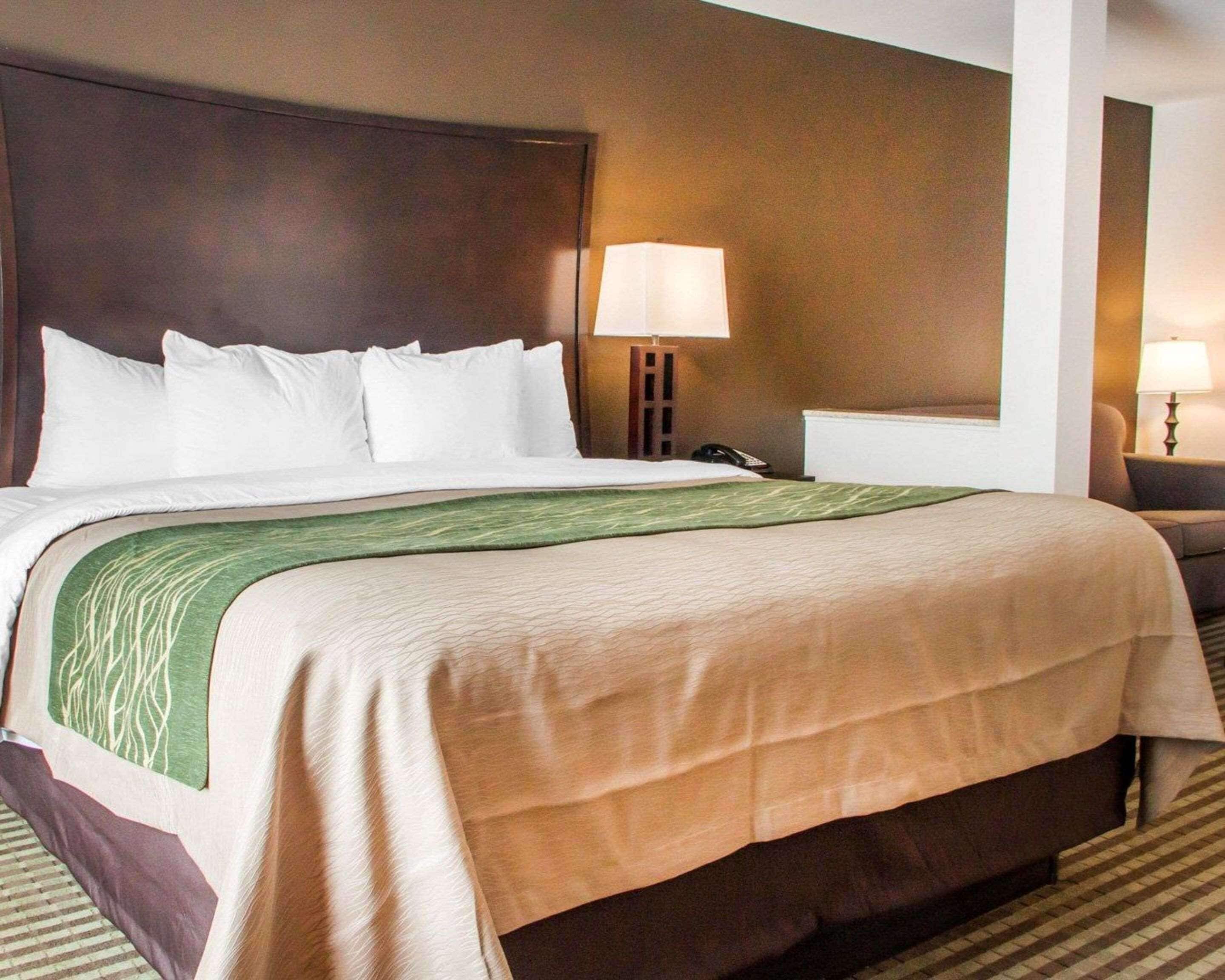 A hotel room with a large bed, a nightstand, a lamp, and a chair.