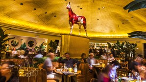 Ein Restaurant mit einer großen goldenen Decke, einer roten Skulptur eines Pferdes und Gästen, die an Tischen sitzen.