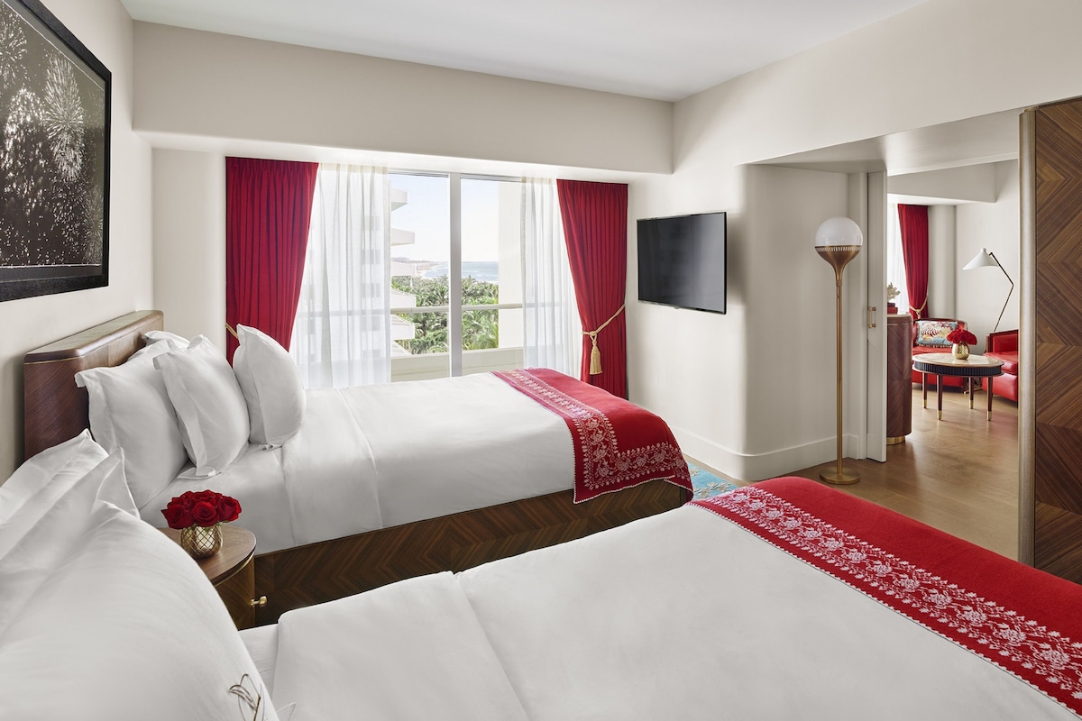 A hotel room with two beds, a TV, a red and white decor theme, and a view of the outdoors.