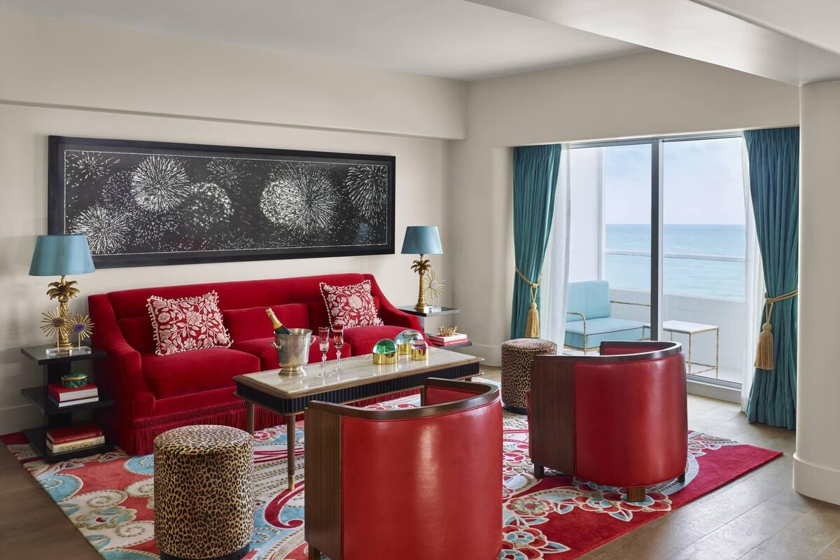 A red sofa, two red side tables, a coffee table, a leopard print ottoman, and a large window with a view of the ocean.