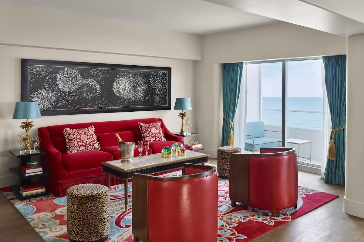 Ein rotes Sofa, zwei rote Beistelltische, ein Couchtisch, ein Ottoman im Leopardenmuster und ein großes Fenster mit Blick auf den Ozean.