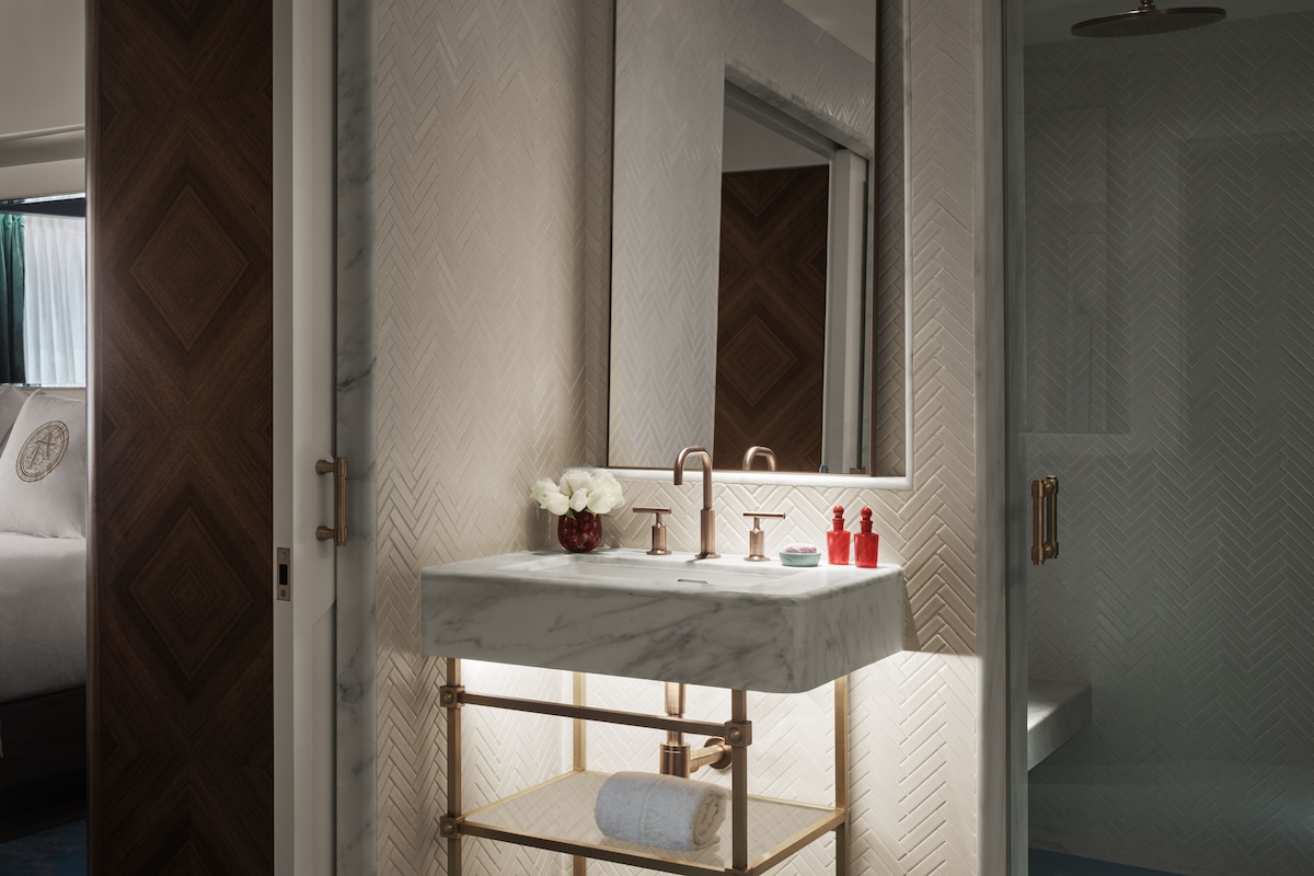 A bathroom with a marble sink, a mirror, a shower, and a towel rack.