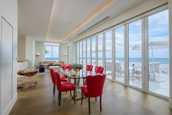 A spacious dining area with a glass table and red chairs, large windows with a view of the sea, and a modern interior design.