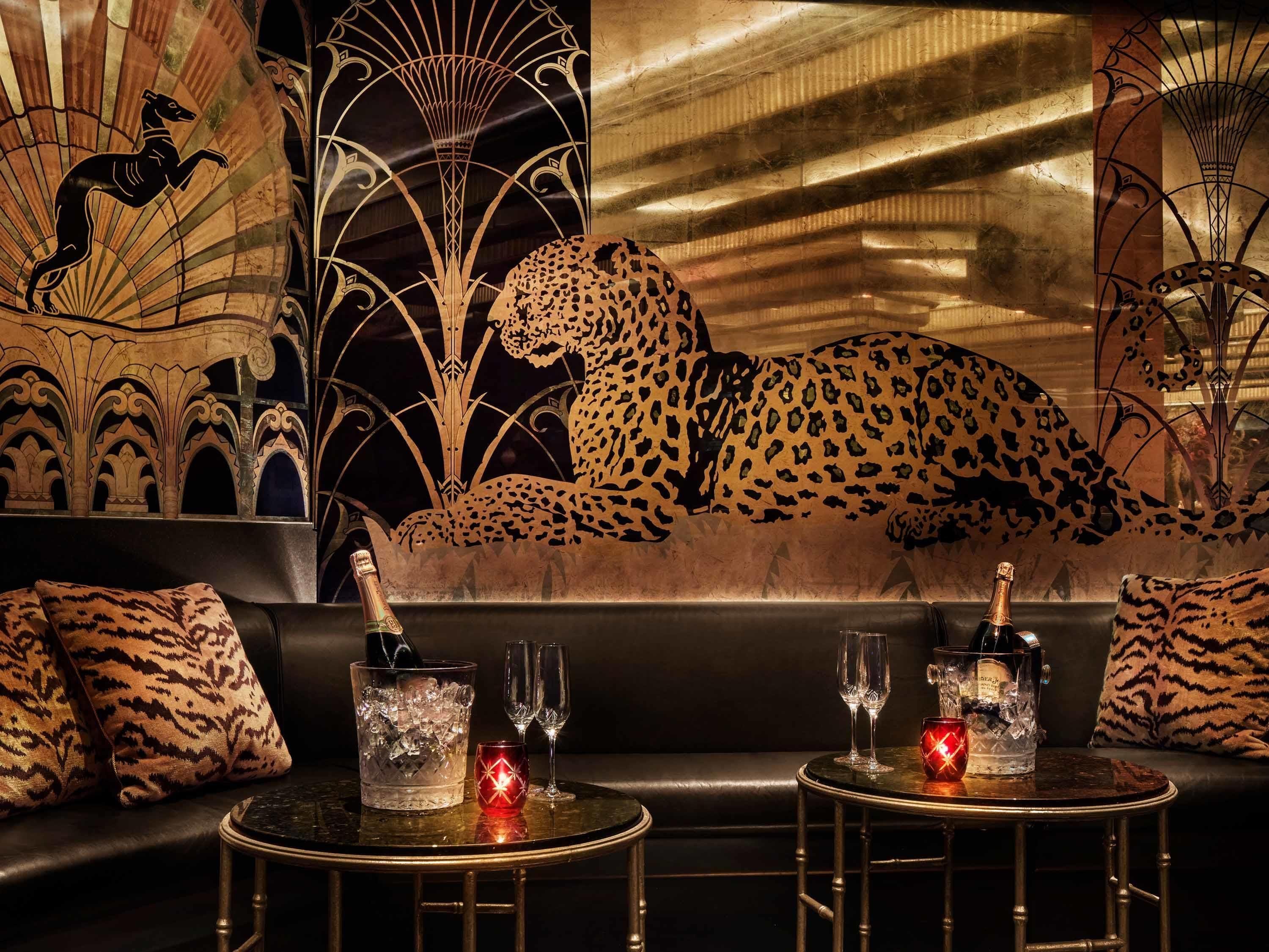A luxurious lounge area with a leopard mural, ice buckets, champagne, and glasses on a leather couch and tables.