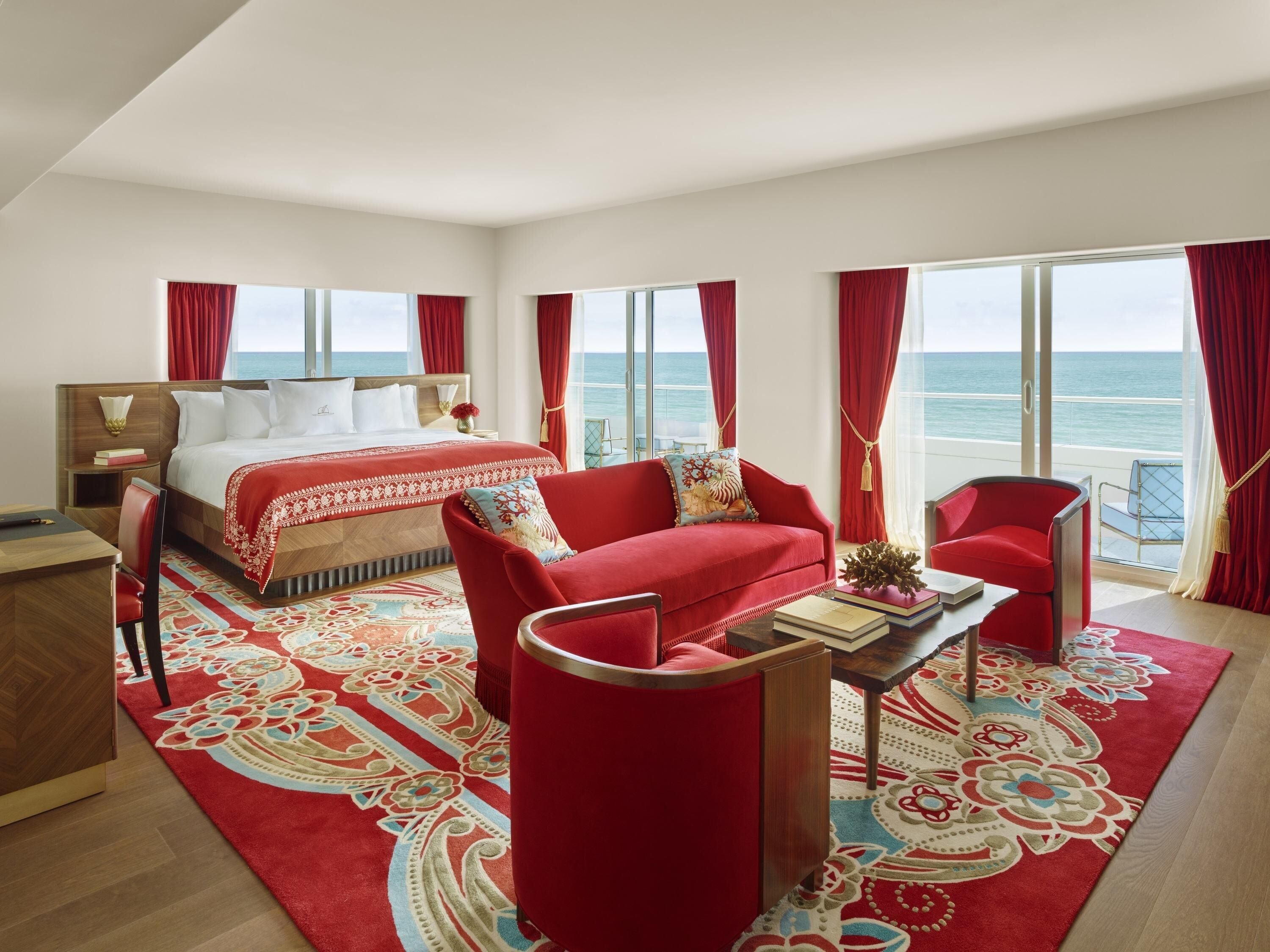 A hotel room with a bed, a red sofa, a coffee table, and a view of the sea.