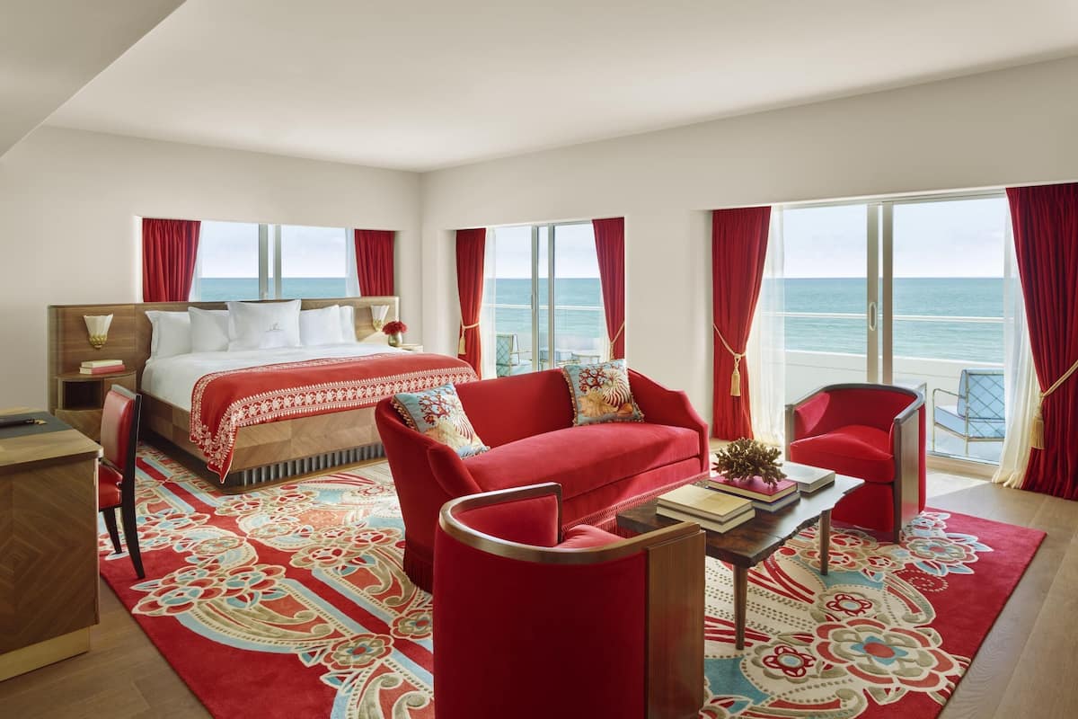 A hotel room with a bed, a red sofa, a coffee table, and a view of the sea.