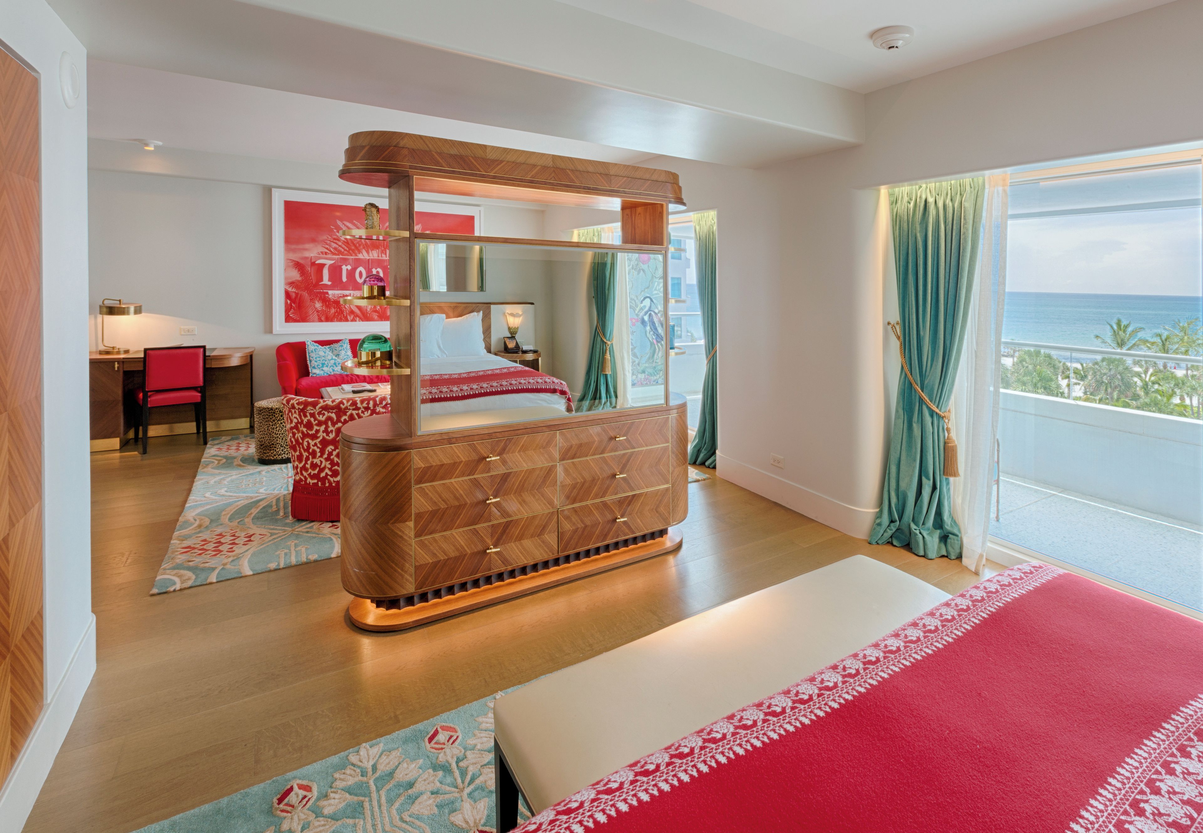 A modern bedroom with a large bed, a wooden headboard, a desk, and a view of the ocean.