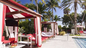 A poolside area with red and white lounge chairs, a small table with a fruit bowl, and a pool.
