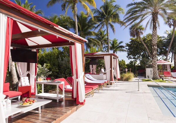 A poolside area with red and white lounge chairs, a small table with a fruit bowl, and a pool. - Faena Miami Beach (Miami Beach)