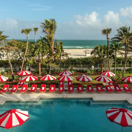 A pool area with red and white striped umbrellas, sun loungers, and a view of the beach and ocean.