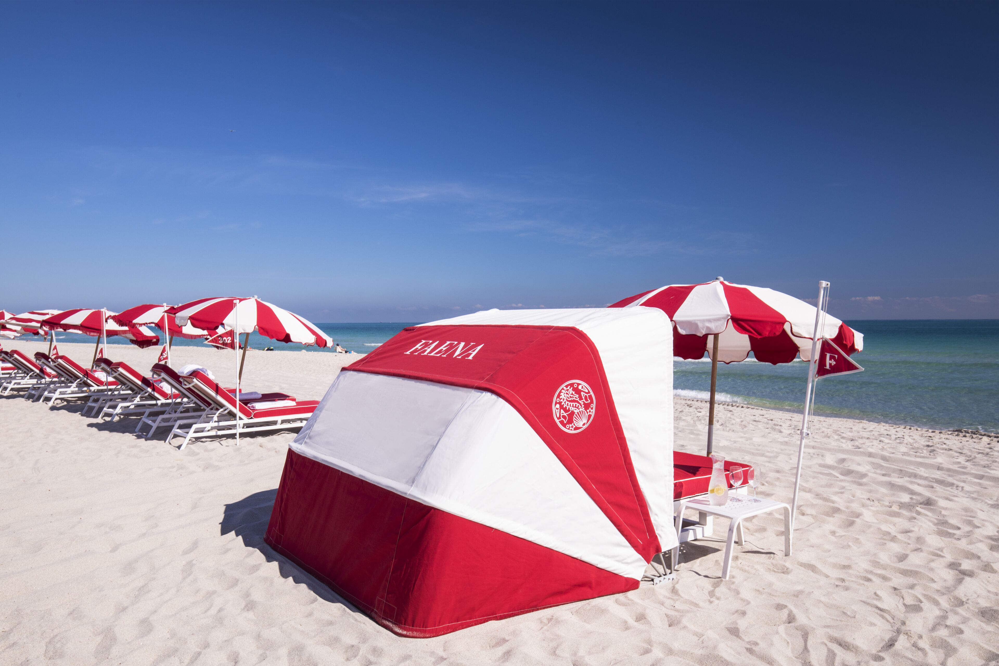 A beach with red and white beach umbrellas, lounge chairs, and a tent labeled "ELENA".