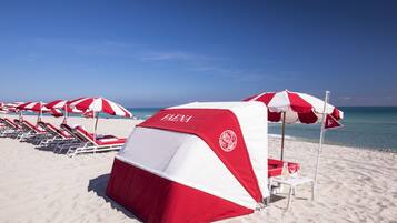 A beach with red and white beach umbrellas, lounge chairs, and a tent labeled "ELENA".