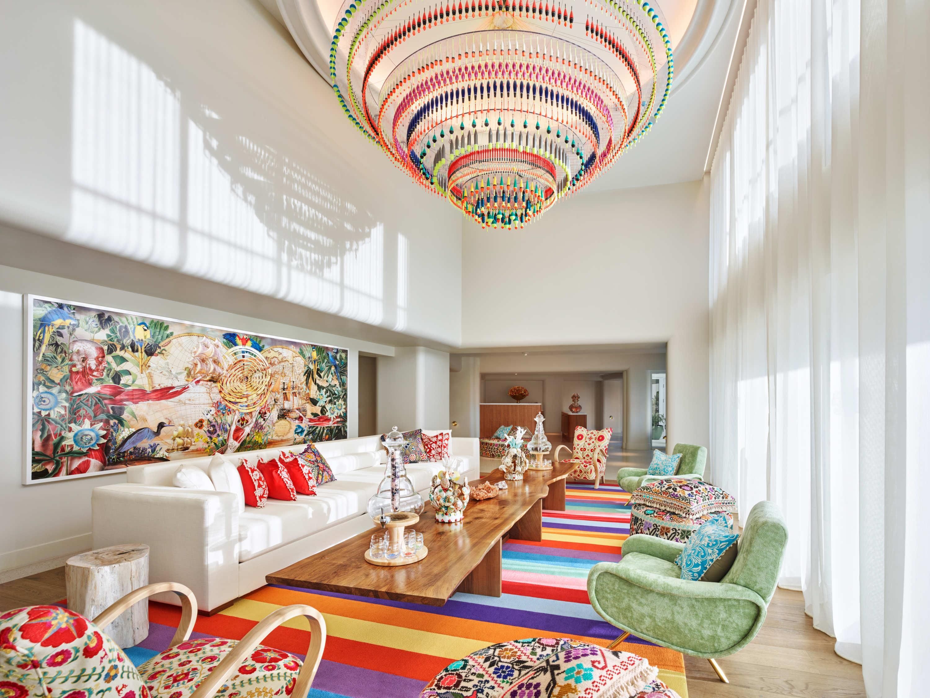 Uma sala de estar ampla com um tapete grande e colorido, um sofá branco, uma mesa de centro de madeira e um lustre vibrante.