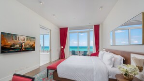 Ein Hotelzimmer mit einem großen Bett, einem an der Wand befestigten Fernseher, Meerblick und einem roten Vorhang.