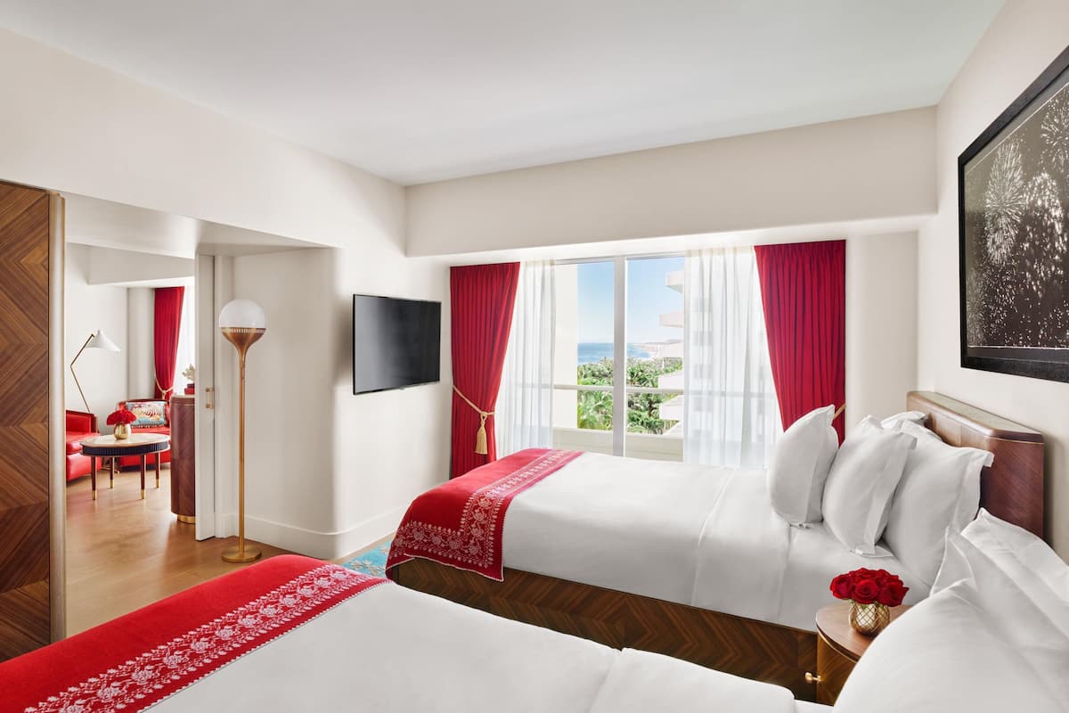 Ett hotellrum med två sängar, en TV, ett skrivbord och utsikt över havet.