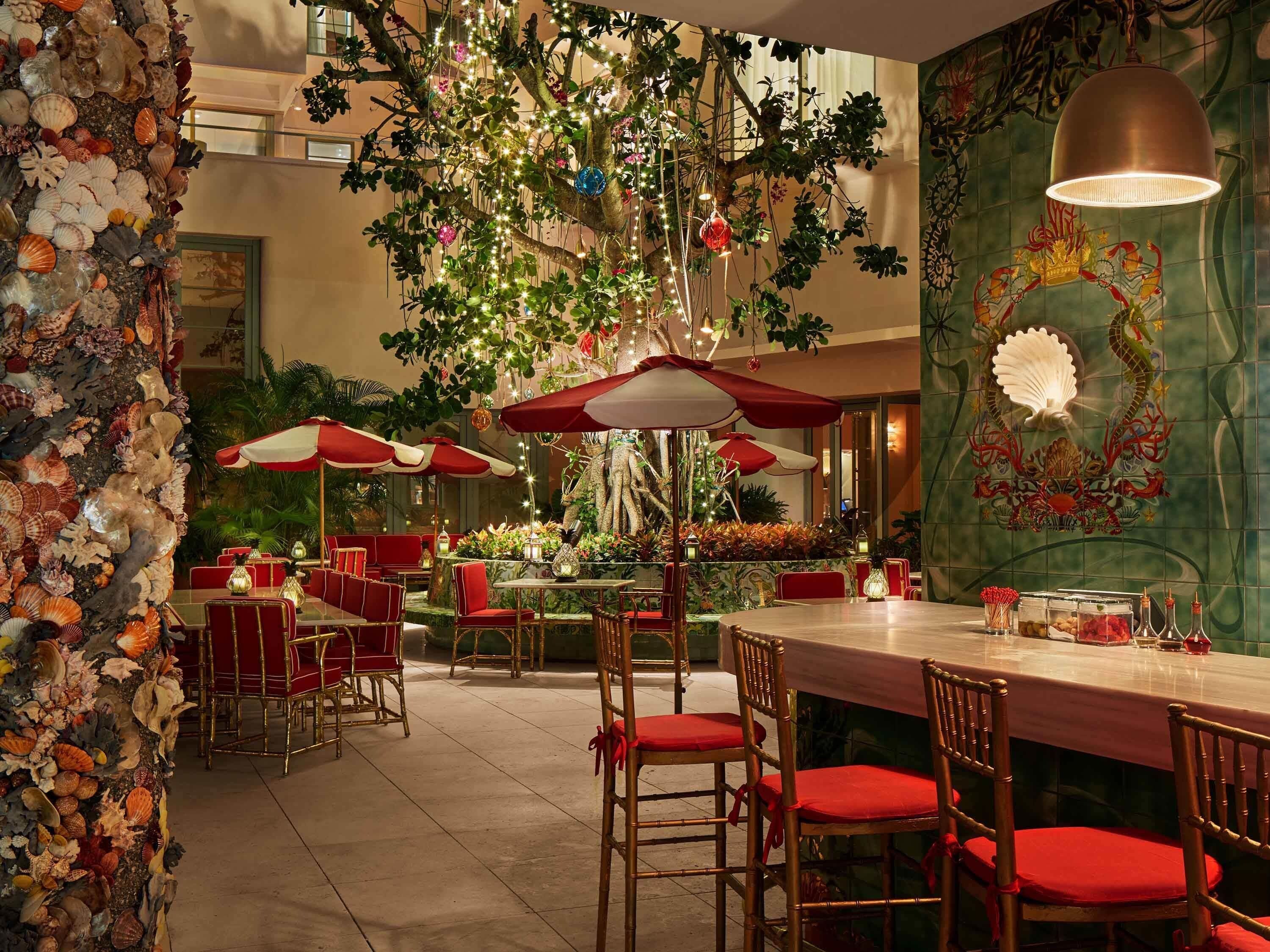 A restaurant with red and white umbrellas, bamboo chairs, and a decorative wall with shells.