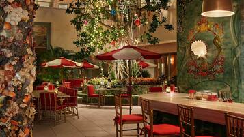 A restaurant with red and white umbrellas, bamboo chairs, and a decorative wall with shells.
