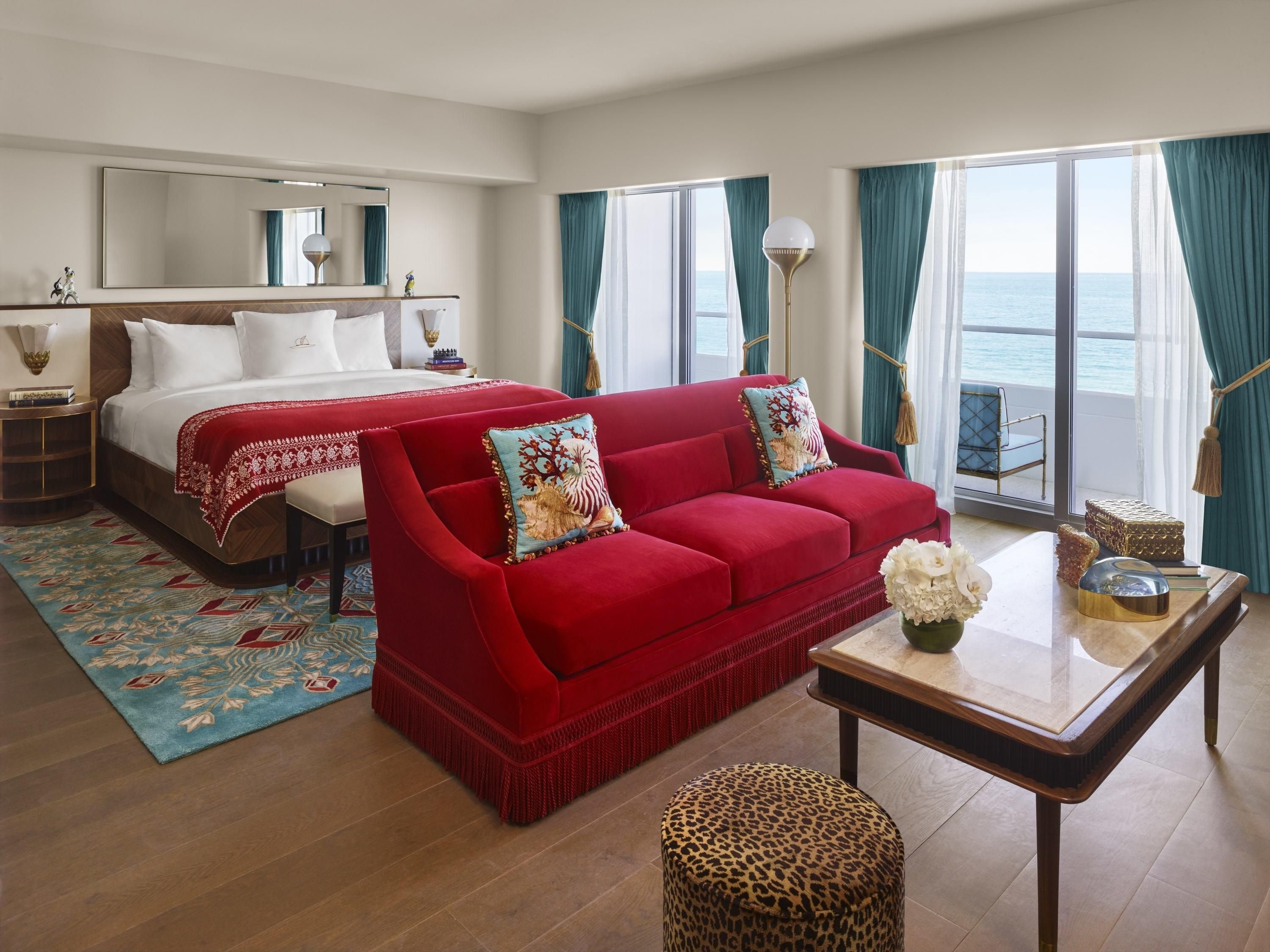 Une chambre d’hôtel avec un lit, un canapé rouge, une table basse et une vue sur la mer.