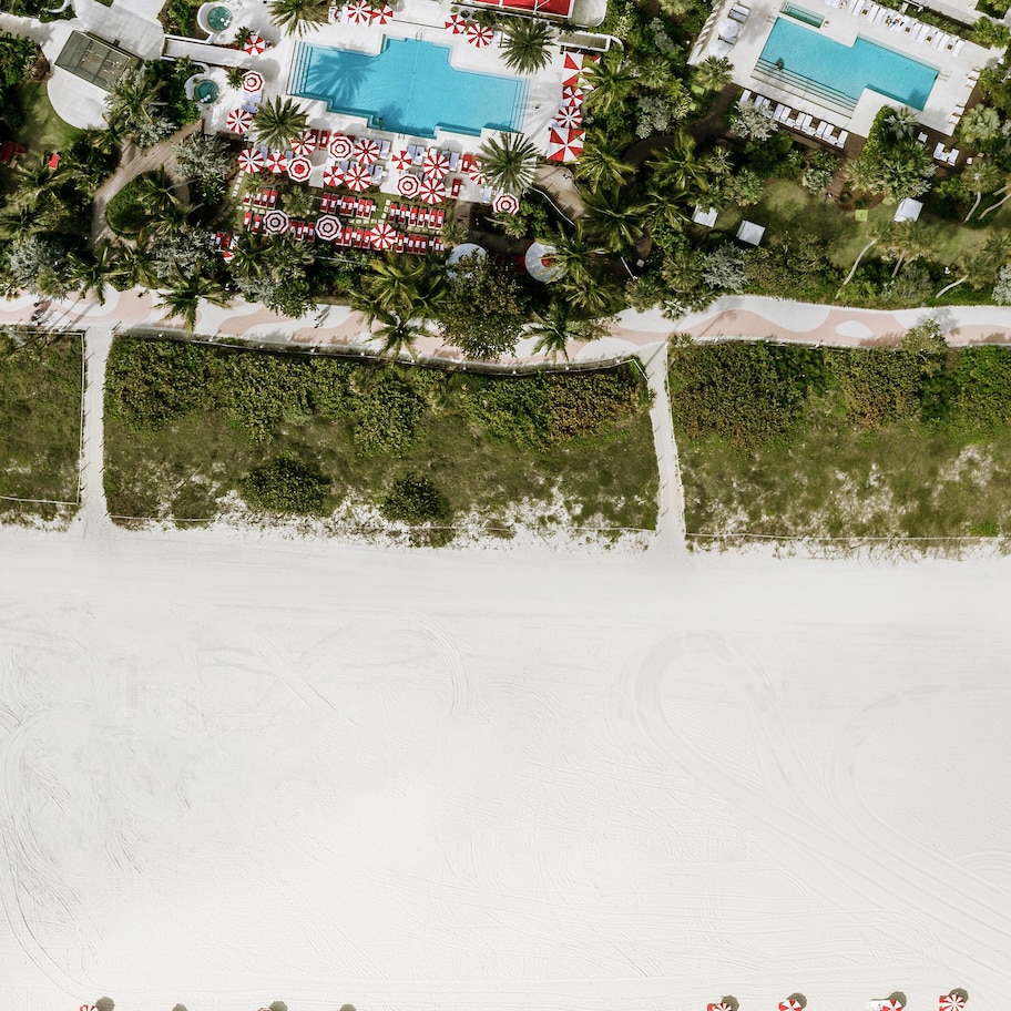 An aerial view of a beach resort with a large pool, sun loungers, and a clear view of the ocean.