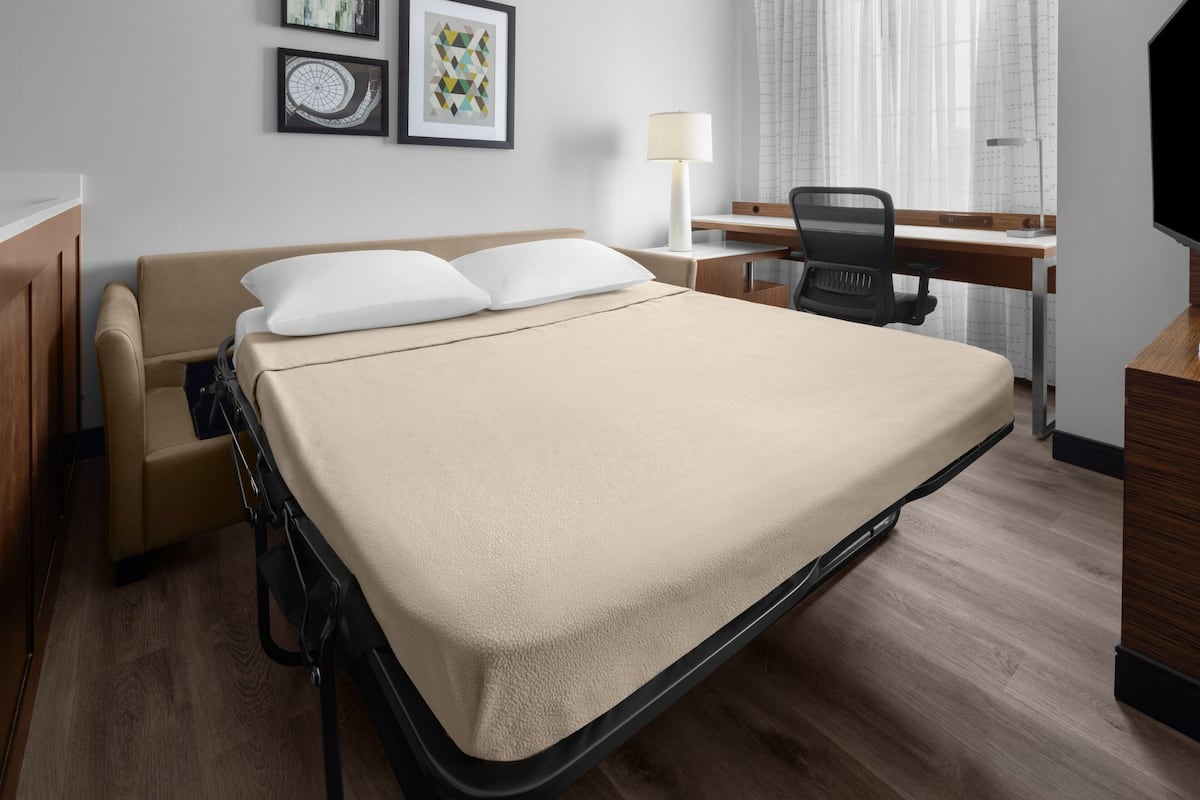 A hotel room with a bed, a desk, a chair, and a TV.