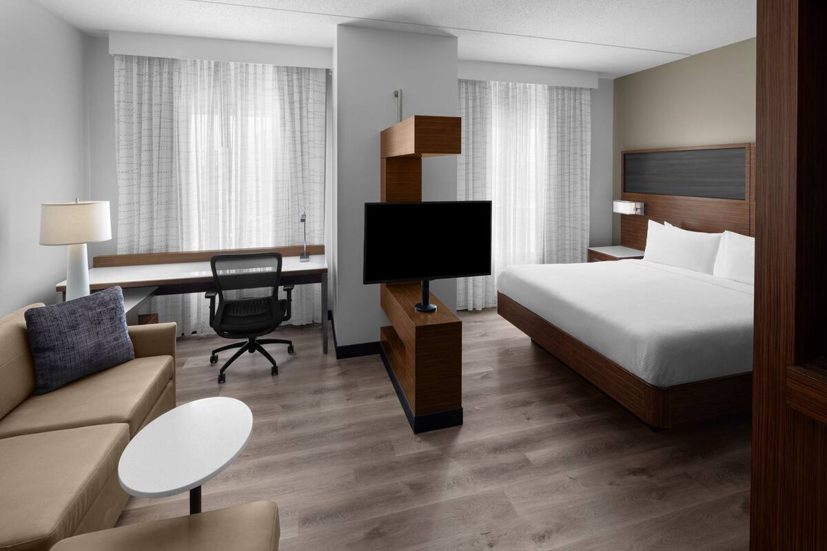 A modern hotel room with a bed, a desk, a chair, a television, and a small table.