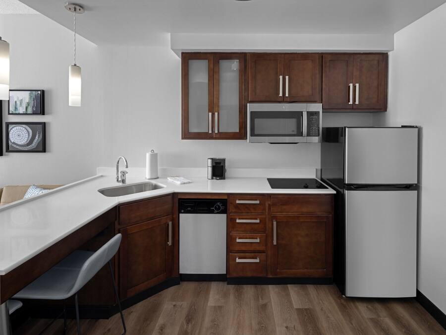 A modern kitchen with wooden cabinets, a microwave, a refrigerator, a dishwasher, and a bar area with stools.