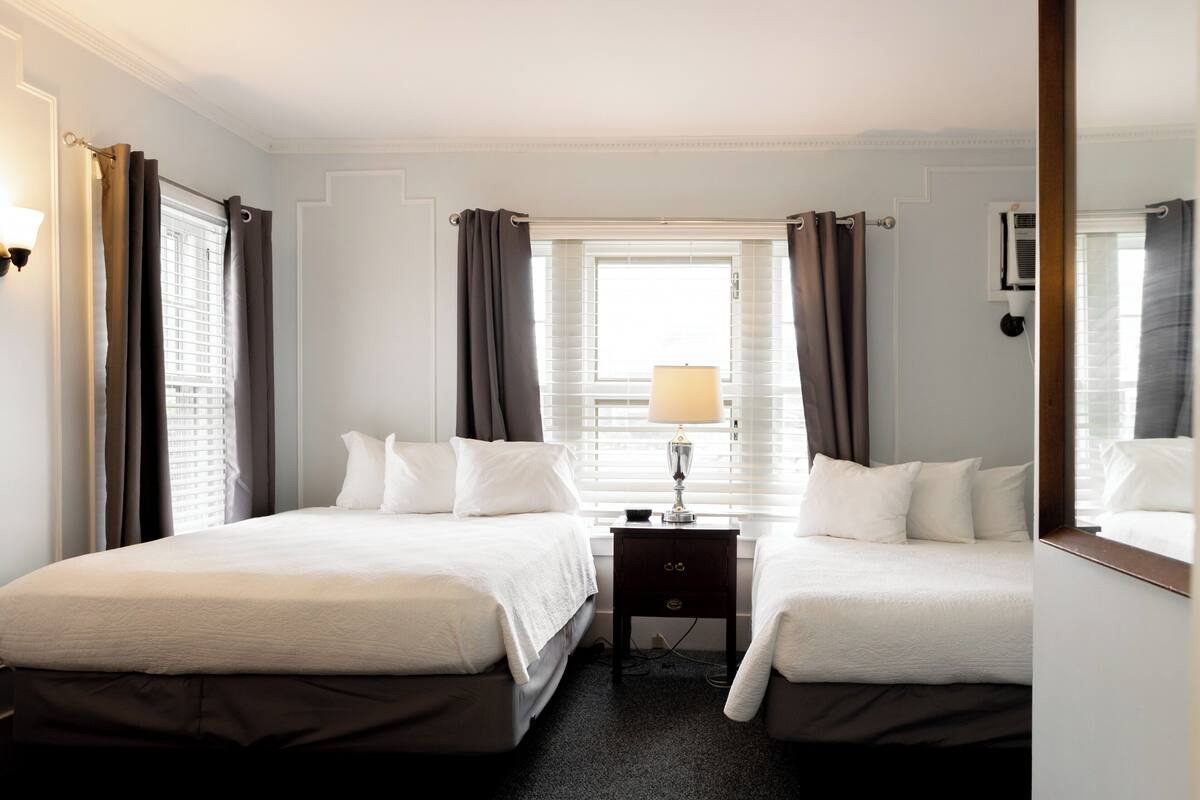 Una habitación de hotel con dos camas, una mesita de noche con lámpara y una ventana con cortinas.