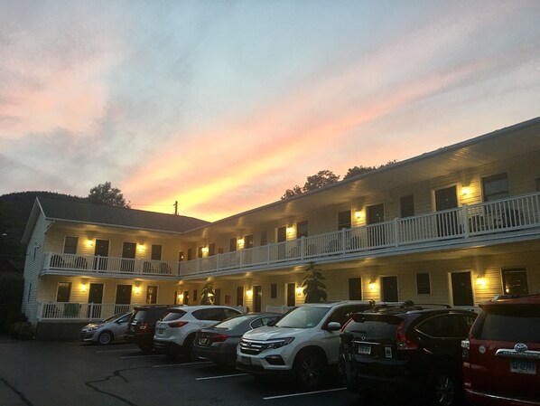 A motel with multiple floors, a parking lot with several cars, and a sunset sky.