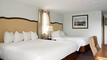A hotel room with two beds, a desk, a chair, a lamp, and a framed picture on the wall.