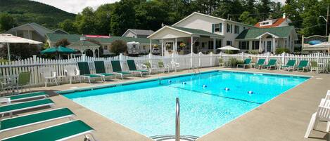 Una piscina al aire libre, sombrillas, sillones reclinables de piscina