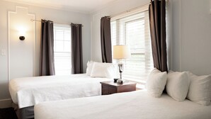 A hotel room with two beds, a nightstand with a lamp, and a window with curtains. - Heritage of Lake George (Lake George)