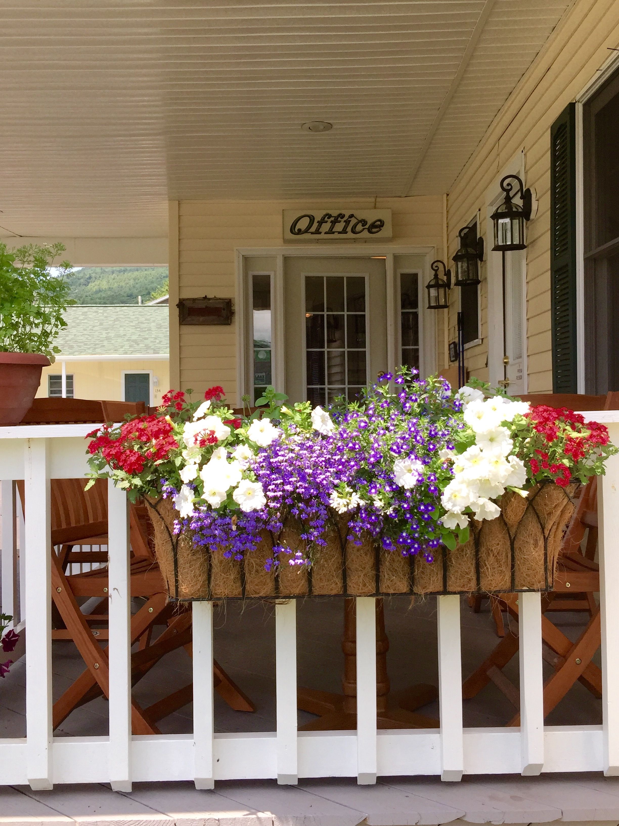 A porch with a sign reading "Office" above a wooden table adorned with flower baskets.
