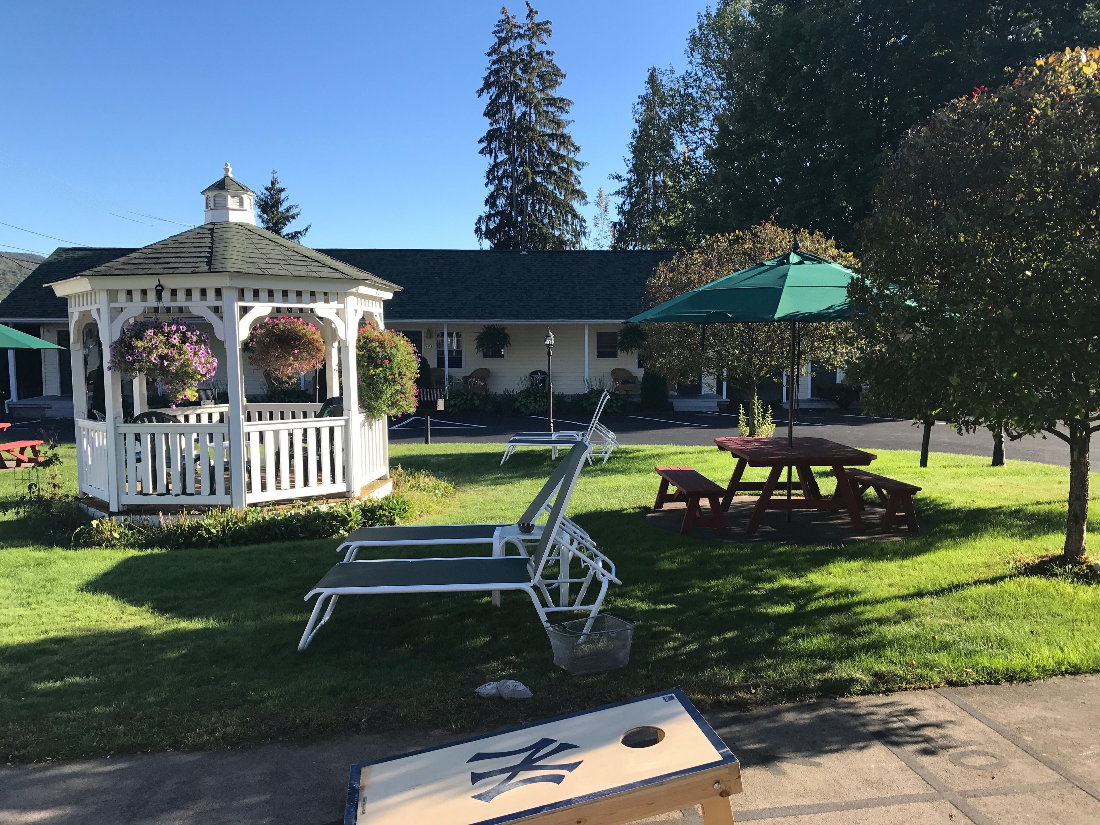 A gazebo with hanging flower baskets, a picnic table, and a lawn chair in a grassy area.