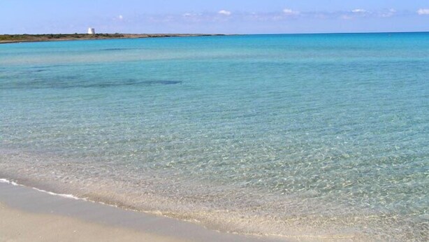 Una playa con agua turquesa cristalina y un edificio blanco a lo lejos.