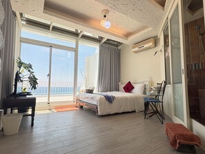 A bedroom with a bed, a desk, a chair, a plant, and a view of the sea. - Ming-Jun Holiday Inn (Hengchun)