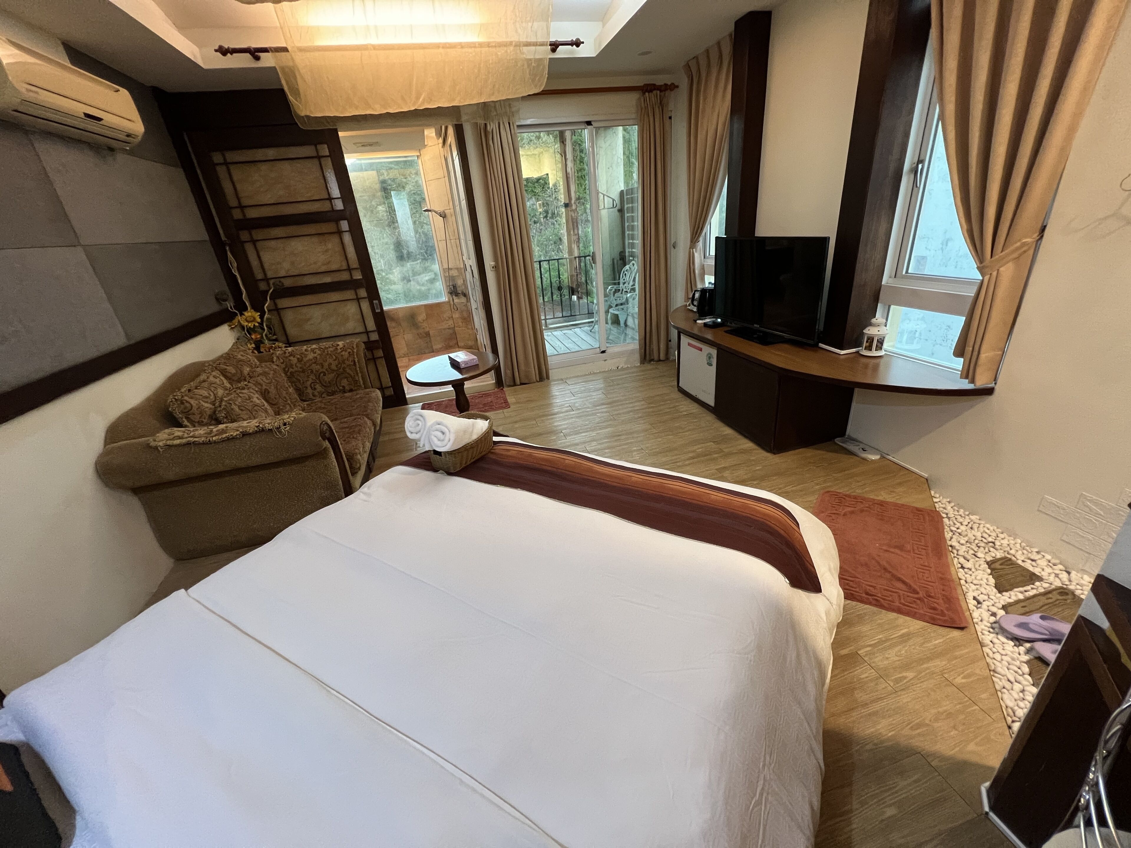 Une chambre d’hôtel avec un grand lit, un canapé, une télévision et un balcon avec des rideaux.