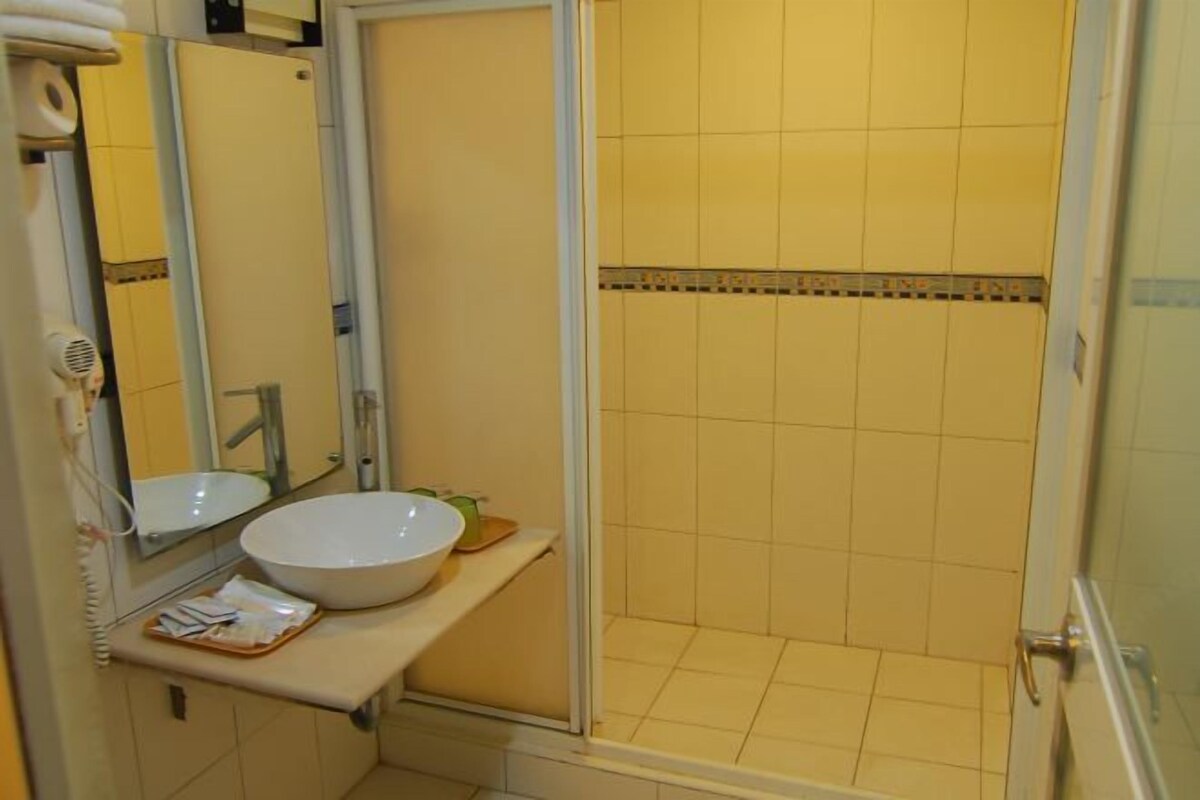 A bathroom with a white sink, mirror, and a shower area with yellow tiles.