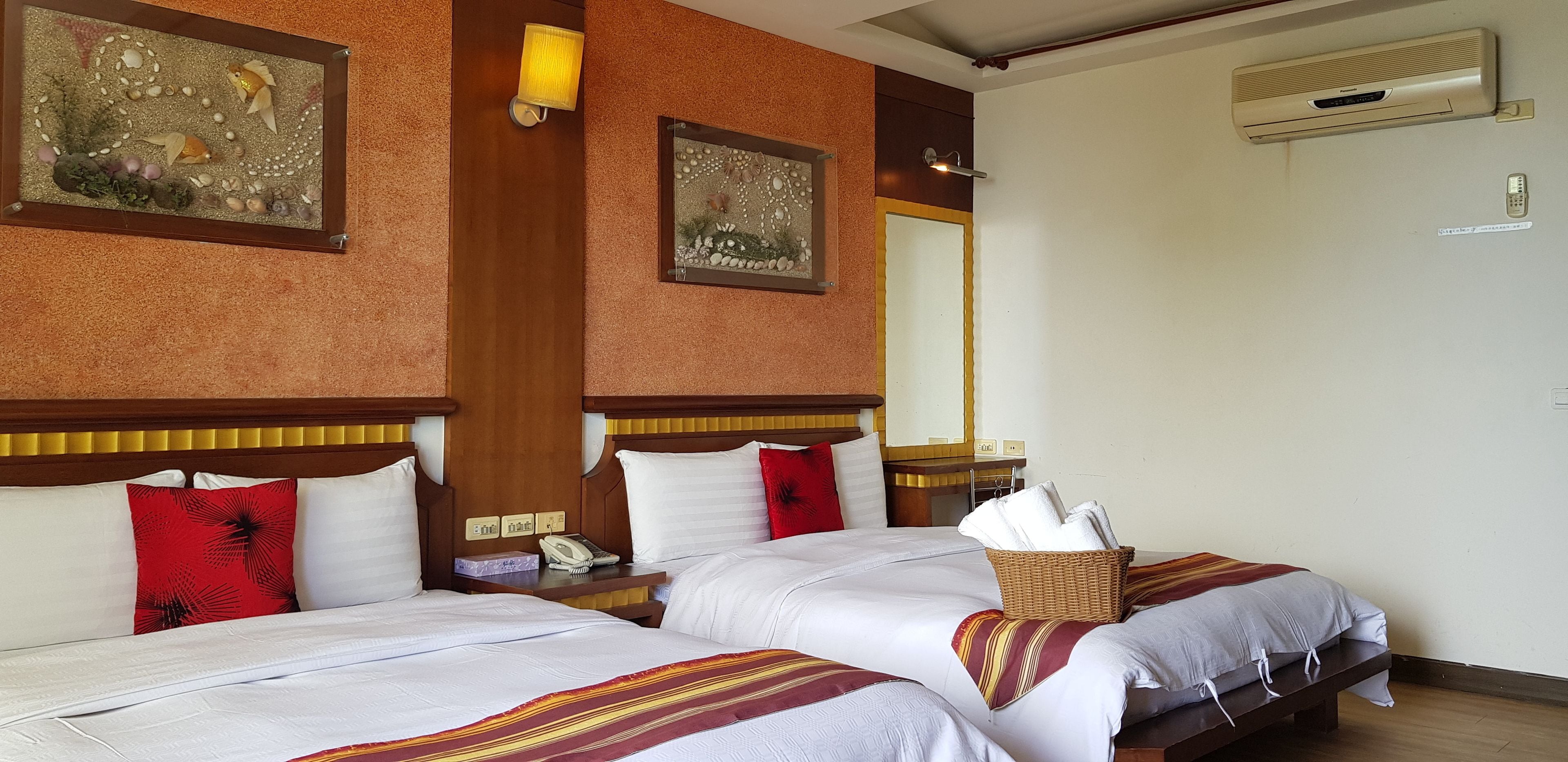 Habitación de hotel con dos camas, una mesita de noche con teléfono, aire acondicionado de pared y un espejo.
