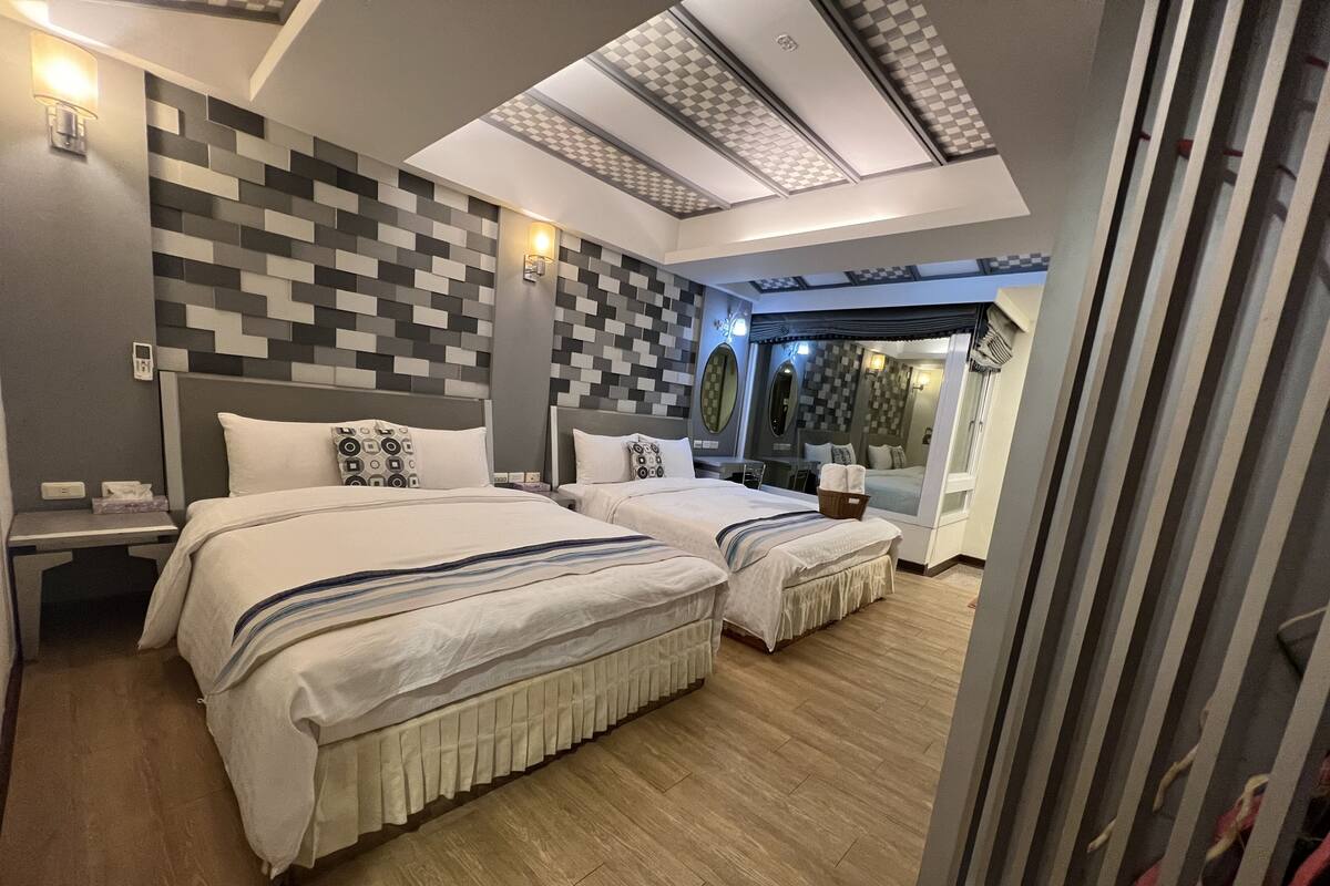 A modern hotel room with two beds, a large mirror, and a view of the outside.