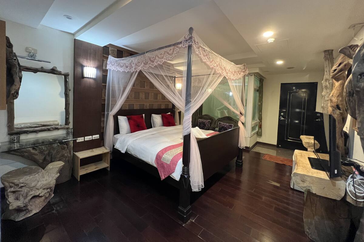 A four-poster canopy bed with a wooden headboard, a small wooden nightstand, and a stone sculpture on the floor.