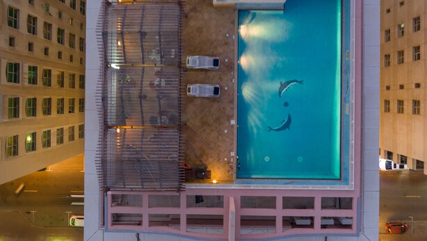 An aerial view of a hotel with a rooftop swimming pool, a covered area with seating, and a parking lot. - La villa Najd Hotel Apartments (Dubai)