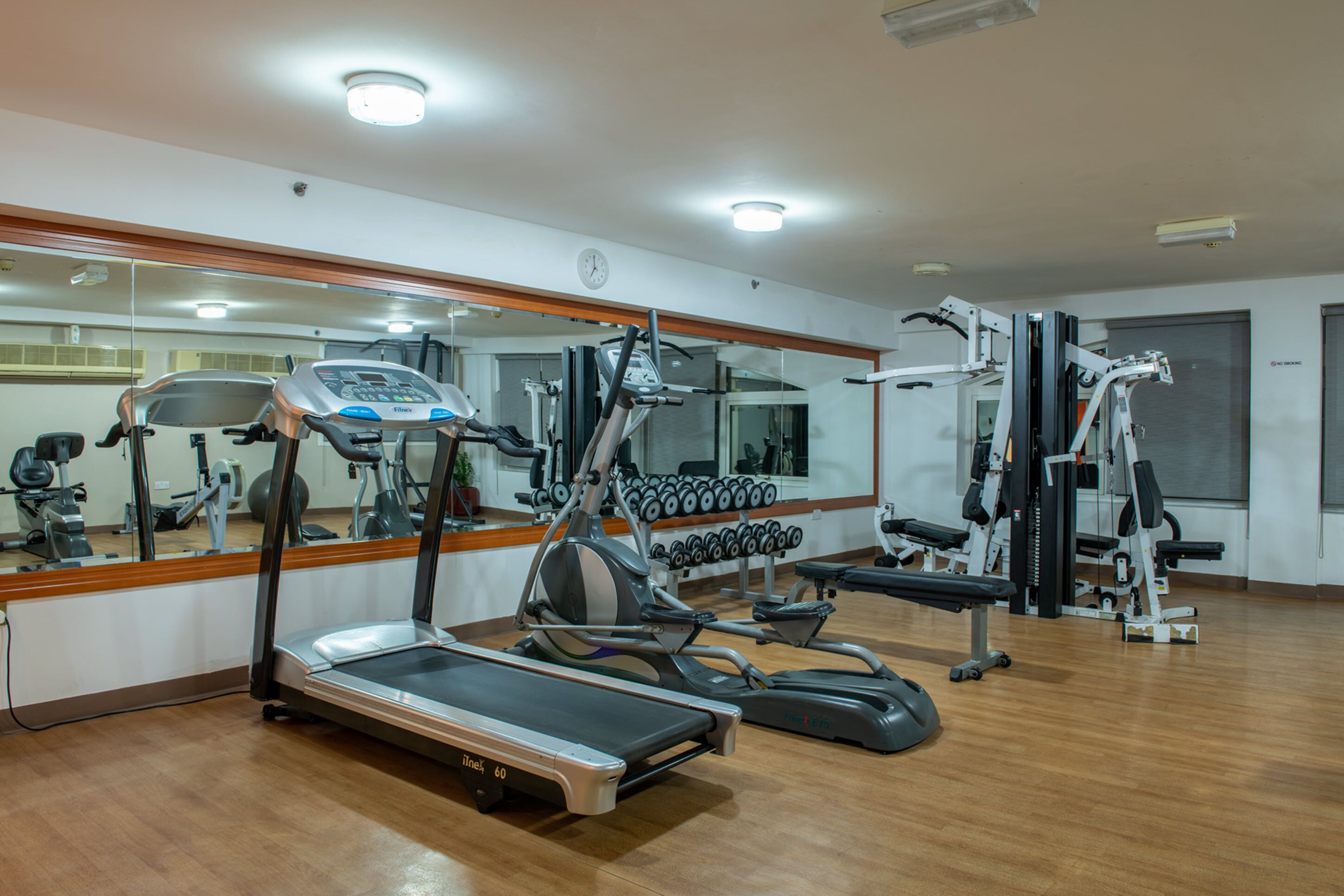 Ein Fitnessraum mit Cardiogeräten, Hanteln und einer Spiegelwand.