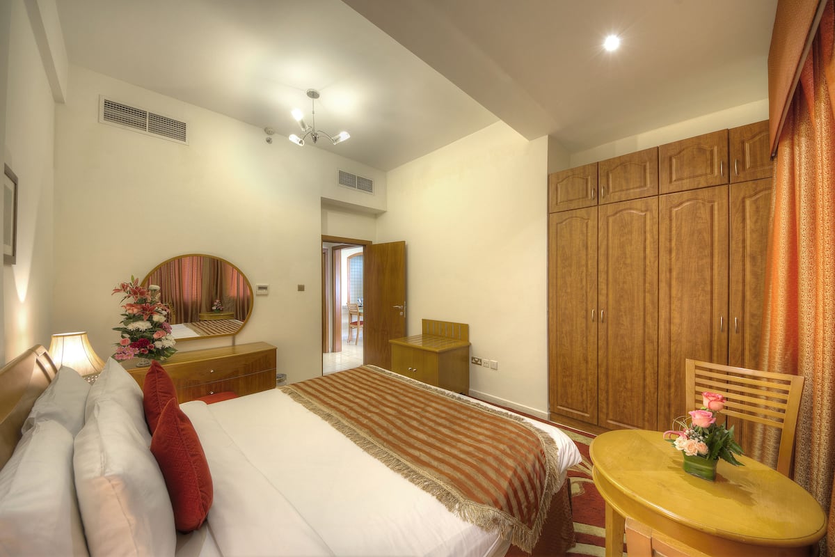A hotel room with a bed, a wooden wardrobe, a round table with a vase of flowers, and a mirror on the wall.