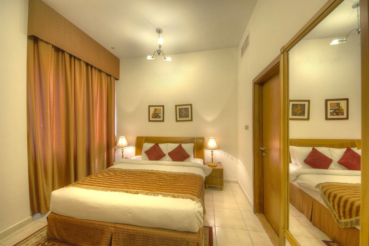 A hotel room with a large bed, two bedside lamps, a mirror, and two framed pictures on the wall.
