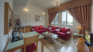 A living room with a glass coffee table, red sofas, a TV, and a dining area with chairs and a table. - La villa Najd Hotel Apartments (Dubai)