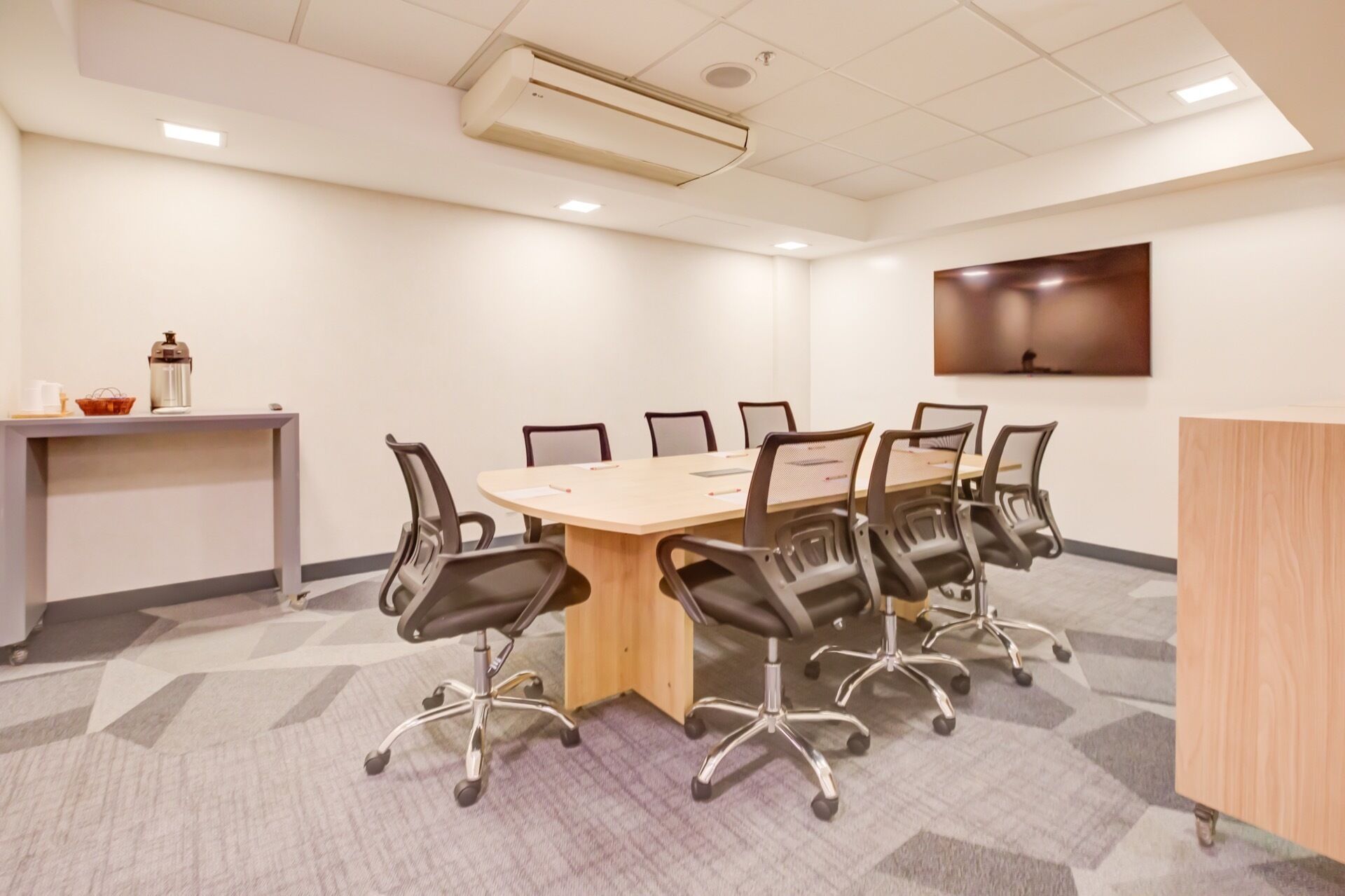 A conference room with a large table, six chairs, a coffee station, and a TV on the wall.