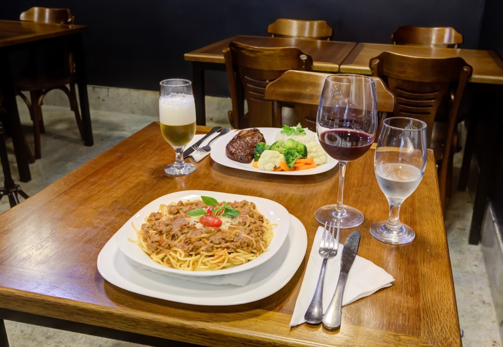 Una mesa de comedor con un plato de espagueti, una copa de vino blanco y una copa de vino tinto.